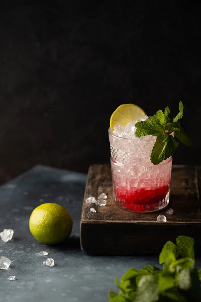 Cocktail rinfrescante con vodka, soda, purea di frutti di bosco, lime, menta e ghiaccio tritato su scatola di legno e fondo scuro. — Foto Stock