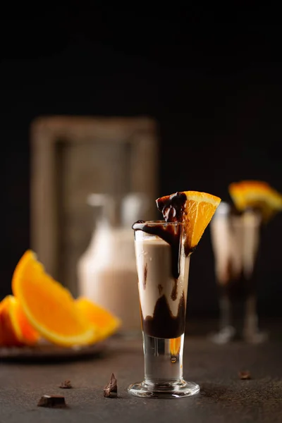 Sweet cocktail in shot glass with chocolate,cream liqueur,fresh oranges on dark background.Close up.Bar menu,recipes. — Stock Photo, Image