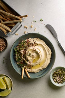 Balkabağı tohumlu Frseh Humus, kekik, nohut, limon ve ekmek çubukları seramik platoda gri sırtüstü..