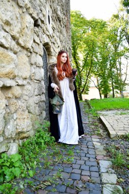 Taş bir kalenin, metal bir kapının ve hapishane penceresinin önündeki kaldırım taşlarının üzerindeki seksi, uzun saçlı genç kız.