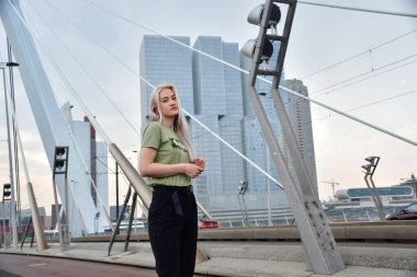 Rotterdam köprüsünde gökdelenli bir fotoğraf çekiminde sarışın.