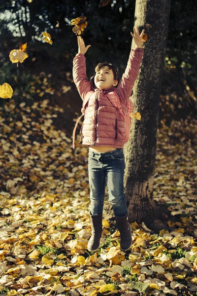 Menina brincando em folhas caídas — Fotografia de Stock