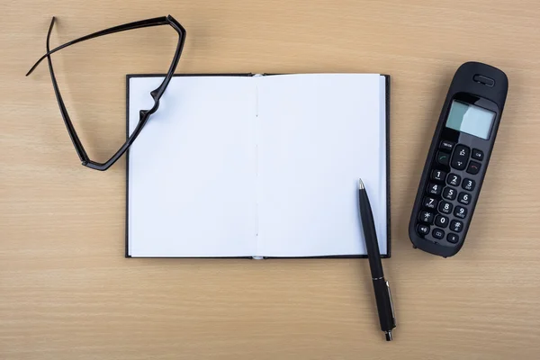 Notitieblok openen en zwarte telefoon op houten textuur. — Stockfoto