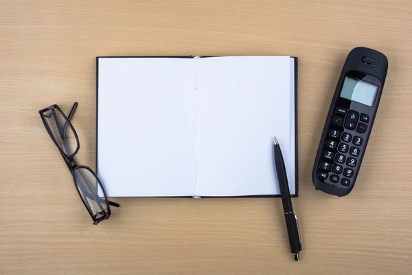 Notebook aberto e telefone preto na textura de madeira — Fotografia de Stock