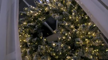 Karlı, ışıkla kaplı Noel çelengi pencereye asılıydı.