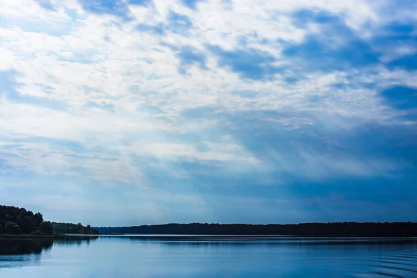 The rays of God in the river landscape. The sun\'s rays shine through the clouds over the water surface and the shore. Copy space.