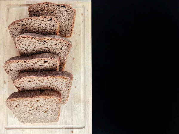 Rodajas de pan de centeno sobre una tabla de madera sobre un fondo negro —  Fotos de Stock