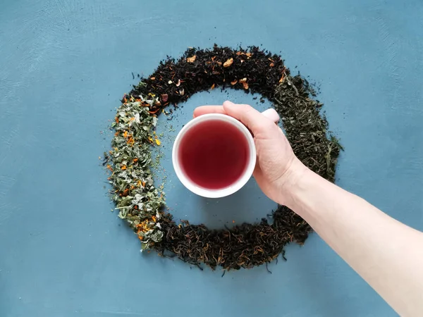 The dial is from different types of dry tea, in the middle of a mug of tea and a hand taking it. Tea party concept. — Stock Photo, Image