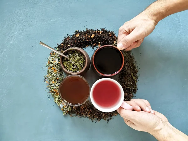 4 tazas con diferentes tipos de té y manos recogiendo 2 tazas — Foto de Stock