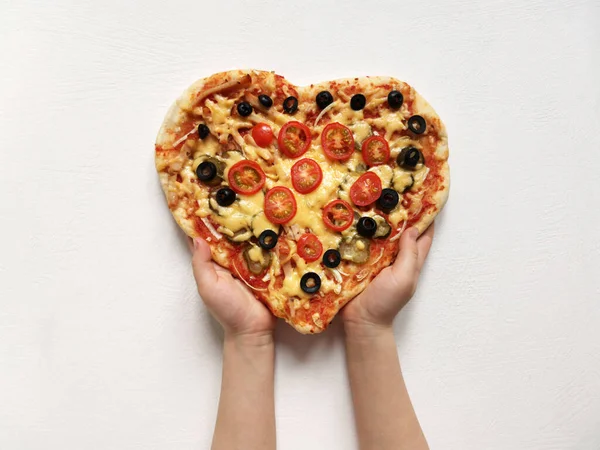 Uma criança segura uma pizza em forma de coração feita com suas próprias mãos. 14 de fevereiro e conceito de feriado do dia das mães — Fotografia de Stock