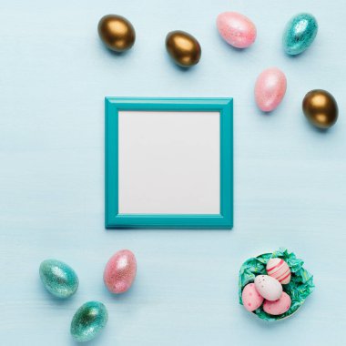 Altın, mavi pastel arka planda parlak Paskalya yumurtaları, metin için yeri olan koyu mavi çerçeve. Düz konum resim kompozisyonu, üst görünüm. Paskalya dekorasyonu, folyo minimalist yumurta tasarımı, modern kart şablonu.