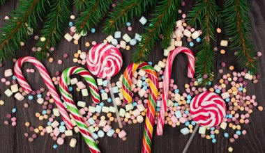 Renkli şekerler, lolipoplar, lokumlar, şeker kamışları ve tahta arka planda firavun ağacı dalları. Üst görünüm, boşluğu kopyala. Tatil Noel tatlı konsepti.