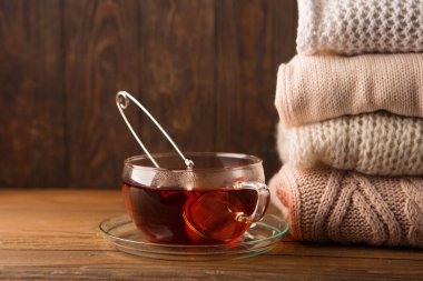 Sıcak örülmüş süveter yığını ve ahşap arka planda bir fincan sıcak çay. Uzayı kopyala, seçici odaklanma. Kış Noel zamanı konsepti