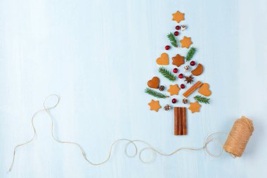 Zencefilli kurabiyelerden, tarçınlardan, kozalaklardan, köknar dallarından ve mavi arka planda kızılcıklardan yapılmış Noel ağacı. Sıfır israf Noel ve yeni yıl kavramı. Düz konum, boşluk kopyala, üst görünüm.