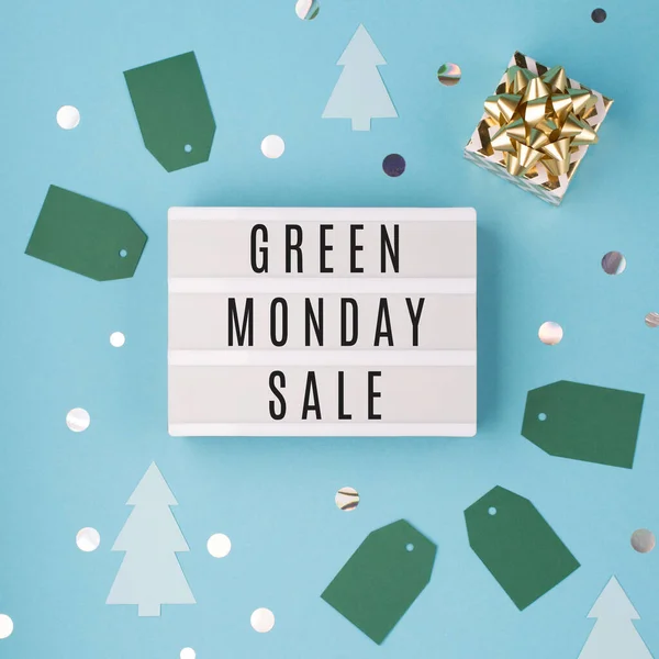 Green Monday sale text on white Lightbox with gold gift box and Christmas decorations on blue paper background. Design for promotion of winter end of year sale. Top view, copy space.