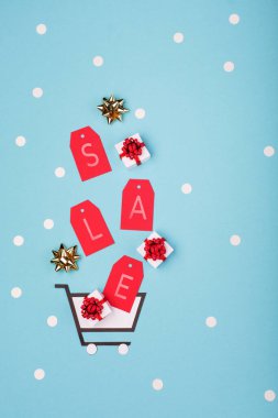 Süper Satış Günü ya da Bekarlar Günü konsepti. Alışveriş arabası, hediye kutuları ve mavi kağıtta kırmızı etiketler. Çin 'den online alışveriş. Üst görünüm, düz görünüm, kopyalama alanı.