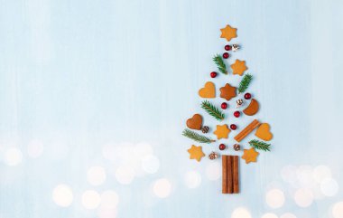 Zencefilli kurabiyelerden, tarçınlardan, kozalaklardan, köknar dallarından ve mavi arka planda kızılcıklardan yapılmış Noel ağacı. Sıfır israf Noel ve yeni yıl kavramı. Düz konum, boşluk kopyala, üst görünüm.