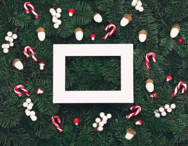 Noel tatili yeni yıl kutlaması kartı. Xmas kırmızı ve beyaz süslemeler, boş beyaz çerçeve, şeker kamışı, mantar, Noel ağacı dallarında meşe palamudu. Düz konum, üst görünüm, kopyalama alanı.