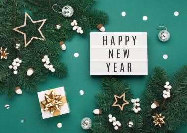 Hediye kutusu, bayram gümüşü ve altın madalyaları, yeşil Noel ağacı dallarında meşe palamudu olan beyaz ışık kutusu üzerine Mutlu Yıllar mesajı. Düz konum, üst görünüm, kopyalama alanı. Şenlikli kış zamanı.