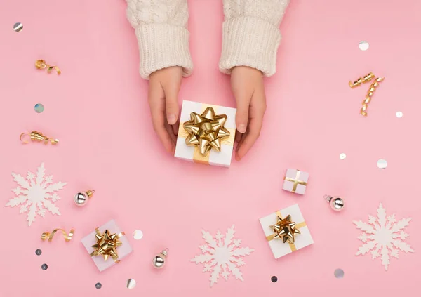 女性の手は 金や銀の装飾 雪の結晶とクリスマスのお祝いのパステルピンクの背景に白いギフトボックスを保持 ホリデークリスマス 新年のコンセプト フラットレイアウト トップビュー コピースペース — ストック写真