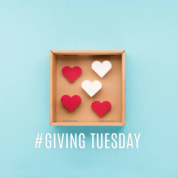 Giving Tuesday, global day of charitable giving after Black Friday shopping day. Charity, give help, donations support concept. Text message, gift box, red hearts on blue background.