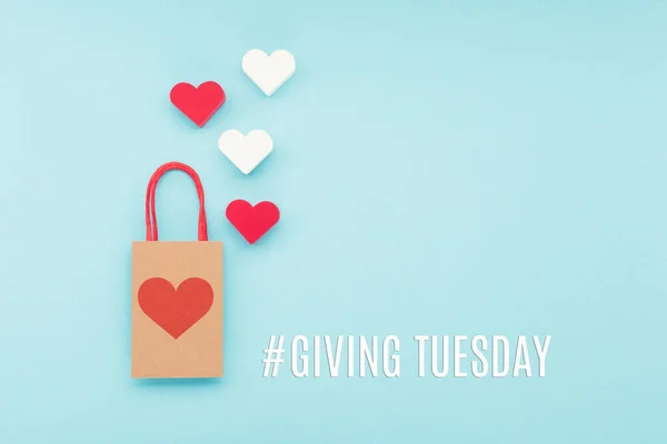 Giving Tuesday, global day of charitable giving after Black Friday shopping day. Charity, give help, donations support concept with text message, red  hearts and shopping bag on blue background.