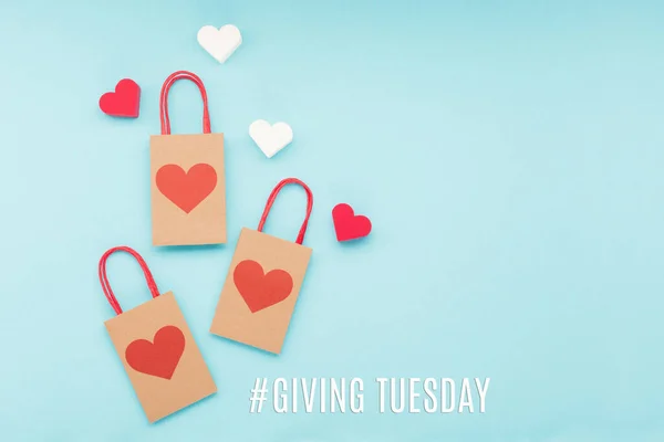 Giving Tuesday, global day of charitable giving after Black Friday shopping day. Charity, give help, donations support concept with text message, red  heart and shopping bags on blue background.
