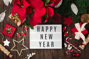 Kırmızı çiçekli beyaz ışık kutusu, Noel süslemeleri, koyu ahşap arka planda hediye kutuları. Düz konum, üst görünüm, kopyalama alanı. Şenlikli el yapımı hediye konsepti