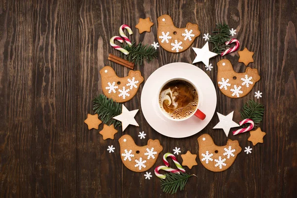 Gingerbread cookies wreath with cup of coffee, Christmas and New Year decor, candy canes, cinnamons on dark wooden background. Concept of holiday winter food.