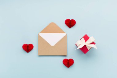 Sevgililer Günü kartı. Kırmızı küçük kağıt kalpler ve pastel mavi arka planda zarflı boş bir kart. Sevgililer Günü konsepti. Düz konum, üst görünüm, kopyalama alanı. 