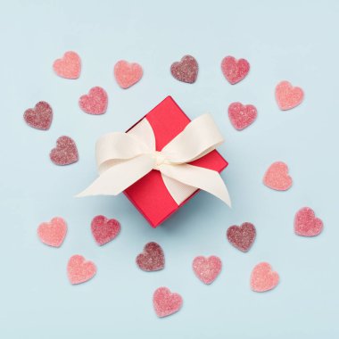 Tatlı şeker kalpler ve mavi arka planda kırmızı hediye kutusu. Sevgililer Günü konsepti. Düz konum, üst görünüm, kopyalama alanı. Sevgililer Günü için bayram tebrik kartı, doğum günü, kadın, anneler günü.