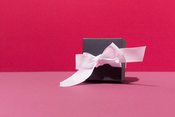 Festive Black gift box with white bow on pink background. Holiday time concept. Gifts for your beloved on your birthday, mother's, sister, woman day.