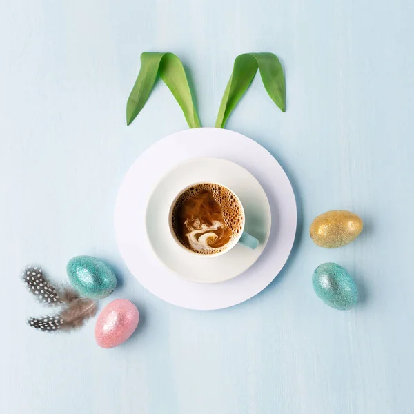 Gold, silver shiny Easter eggs on blue pastel background with cup of coffee. Flat lay image composition, top view. Easter decoration, foil minimalist egg design, modern design template.