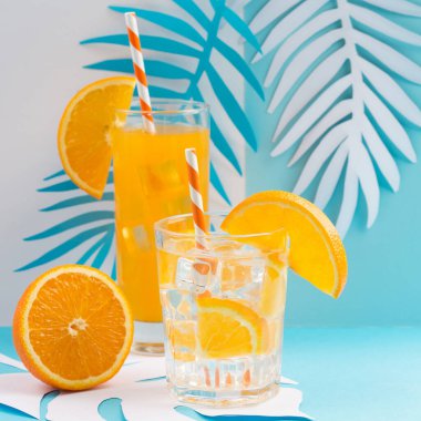 Bardakta soğuk portakal suyu, taze narenciye ve mavi ve beyaz arka planda palmiye yaprakları. Sağlıklı içecek, kopyalama alanı. Tropik yaz konsepti. 