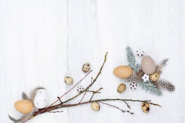 Craft Easter composition with Easter quail eggs in nest, pussy willow branches and cotton flowers on white wooden background. Top view, copy space, flat lay. Easter festive greeting card. 