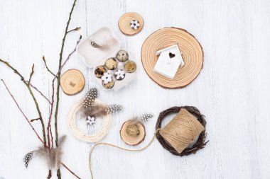 Craft Easter composition with Easter quail eggs in nest, pussy willow branches and cotton flowers on white wooden background. Top view, copy space, flat lay. Easter festive greeting card. 