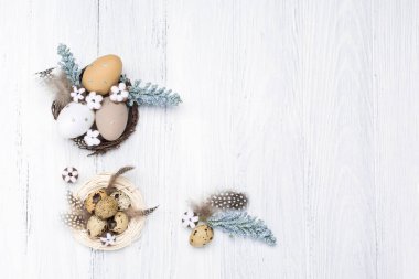 Craft Easter composition with Easter quail eggs in nest, pussy willow branches and cotton flowers on white wooden background. Top view, copy space, flat lay.