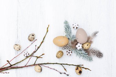 Craft Easter composition with Easter quail eggs in nest, pussy willow branches and cotton flowers on white wooden background. Top view, copy space, flat lay.