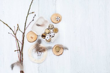 Craft Easter composition with Easter quail eggs in nest, pussy willow branches and cotton flowers on white wooden background. Top view, copy space, flat lay.