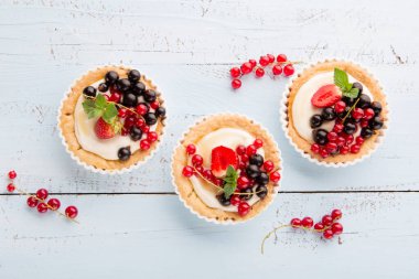 Kremalı ve taze dutlu ev yapımı tartlar olgun kırmızı ve siyah üzümler, mavi rustik ahşap arka planda çilekler, seçici odak. Lezzetli yaz yemekleri..
