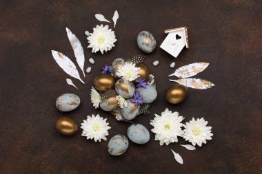 Paskalya bayramı tebrik kartı. Gri mavi altın yumurtalı Paskalya Süslemesi, bıldırcın tüyleri, koyu ahşap arka planda beyaz çiçekler. Paskalya kartı konseptin kutlu olsun. Boşluğu kopyala, üst görünüm.