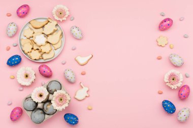 Mutlu Paskalya bayramı tebrik kartları. Ev yapımı Paskalya şekerli kurabiyeler, çikolatalı yumurtalar, pastel pembe arka planda çiçekler. Bayramlık Paskalya kahvaltısı konsepti. Boşluğu kopyala, üst görünüm.