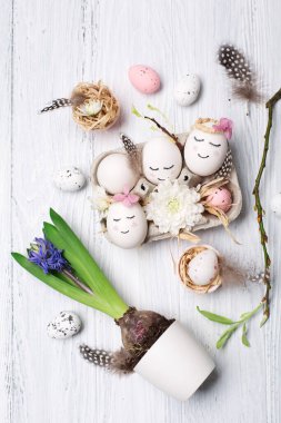 Beyaz şirin yumurtalar, ağaç dalları, bıldırcın tüyleri ve beyaz ahşap arka planda bahar çiçekleri olan tatil yaratıcı Paskalya konsepti. Üst görünüm, boşluğu kopyala. Paskalya bayramı tebrik kartı..