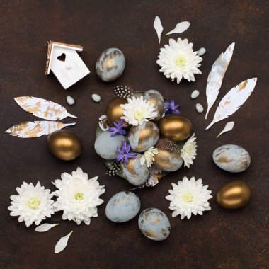 Paskalya bayramı tebrik kartı. Gri mavi altın yumurtalı Paskalya Süslemesi, bıldırcın tüyleri, koyu ahşap arka planda beyaz çiçekler. Paskalya kartı konseptin kutlu olsun. Boşluğu kopyala, üst görünüm.