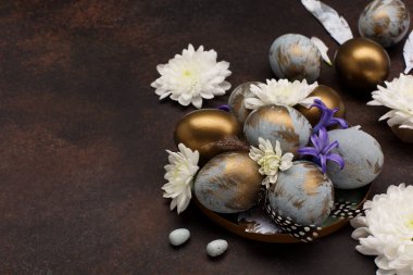 Paskalya bayramı tebrik kartı. Gri mavi altın yumurtalı Paskalya Süslemesi, bıldırcın tüyleri, koyu ahşap arka planda beyaz çiçekler. Paskalya kartı konseptin kutlu olsun. Seçici odak, boşluğu kopyala.