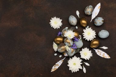 Paskalya bayramı tebrik kartı. Gri mavi altın yumurtalı Paskalya Süslemesi, bıldırcın tüyleri, koyu ahşap arka planda beyaz çiçekler. Paskalya kartı konseptin kutlu olsun. Boşluğu kopyala, üst görünüm.