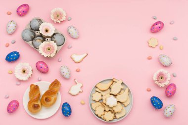 Mutlu Paskalya bayramı tebrik kartları. Ev yapımı Paskalya tavşanı, şekerli kurabiyeler, çikolatalı yumurtalar, pastel pembe arka planda çiçekler. Bayramlık Paskalya kahvaltısı konsepti. Boşluğu kopyala, üst görünüm.