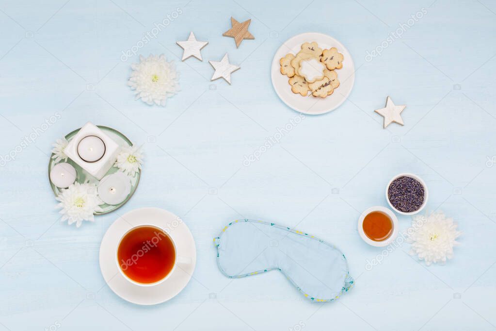 Cotton sleep mask, homemade cookies, cup of herbal tea, dry lavender flowers and candles on blue background. Top view, copy space. Healthy night sleep creative concept in blue colors. 