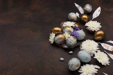 Paskalya bayramı tebrik kartı. Gri mavi altın yumurtalı Paskalya Süslemesi, bıldırcın tüyleri, koyu ahşap arka planda beyaz çiçekler. Mutlu Paskalya kartı kavramı, kopyalama alanı