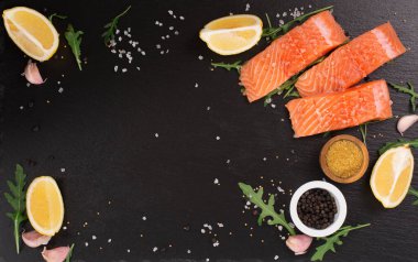 Saf somon fileto, deniz tuzu, limon ve biber ile siyah taş arka planda. Pişirmeye hazır taze balık. Üst görünüm, boşluğu kopyala. Sağlıklı Beyin Gıda Konsepti.